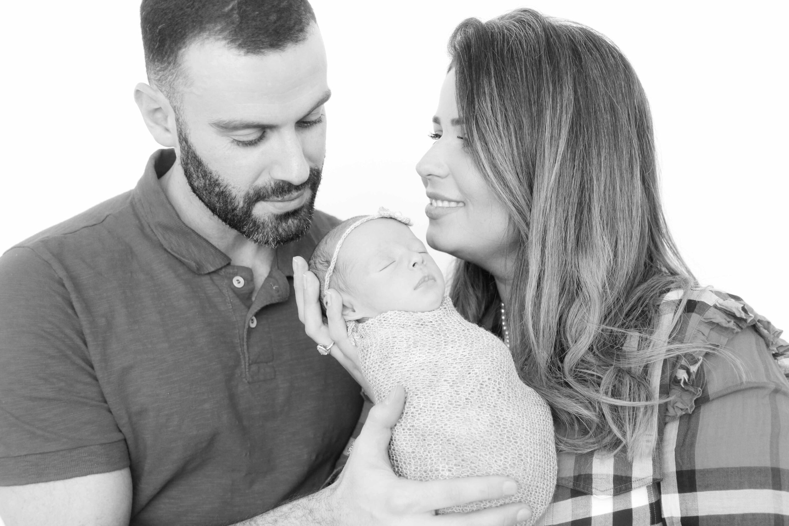 Casal segurando com carinho sua bebê recém-nascida embrulhada em manta, durante ensaio newborn com Estefani Fontes.